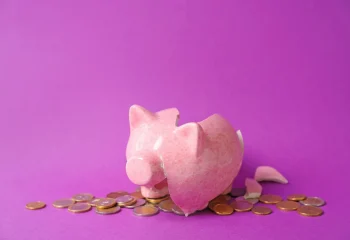 cofrinho rosa quebrado com moedas espalhadas em fundo roxo representando fundo de funil de marketing