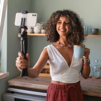 Mulher segurando uma caneca com uma das mãos, enquanto segura um estabilizador com um celular na outra, gravando um conteúdo UGC, ilustrando um artigo de mesmo tema para o blog da Orgânica.