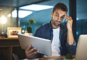 Homem preocupado lendo documento em escrit&oacute;rio moderno com ilumina&ccedil;&atilde;o suave, ilustrando um conte&uacute;do da Org&acirc;nica sobre economia da aten&ccedil;&atilde;o.