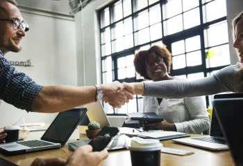 Pessoas em reuni&atilde;o de neg&oacute;cios em um escrit&oacute;rio apertando as m&atilde;os, representando artigo sobre empresas B2B da Org&acirc;nica.