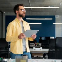 Homem de camisa amarela segurando um tablet no escritório, representando o head de marketing.