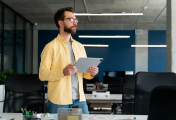 Homem de camisa amarela segurando um tablet no escrit&oacute;rio, representando o head de marketing.