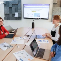 Reunião de equipe em escritório moderno com três mulheres discutindo estratégias de marketing digital, ilustrando um conteúdo da Orgânica sobre ideias de conteúdo.