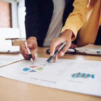 Duas pessoas analisando gráficos e relatórios em uma mesa de escritório, ilustrando um conteúdo da Orgânica sobre marketing estratégico.