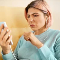 Mulher jovem com cabelo rosa usando fones de ouvido e olhando com expressão preocupada para o celular