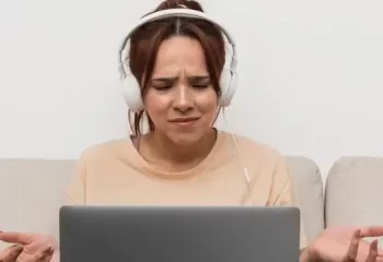 Mulher sentada em sofá, usando fones de ouvido e olhando para laptop com expressão de confusão ou frustração com o erro 404.