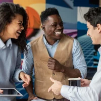 Grupo de colaboradores sorrindo em meio a uma conversa, enquanto a mulher segura um tablet, ilustrando um conteúdo da Orgânica sobre experiências phygital.