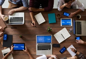 Equipe de trabalho reunida em mesa com laptops, tablets, smartphones, cadernos e caf&eacute;, que ilustram um artigo da Org&acirc;nica sobre tipos de conte&uacute;do.
